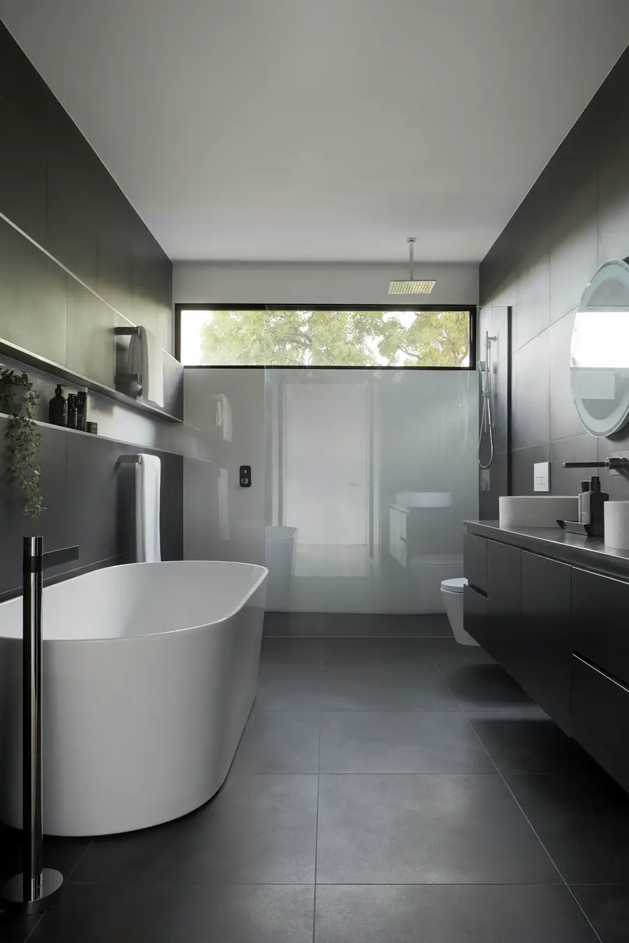 Salle de bains sombre avec baignoire îlot blanche sous une fenêtre haute
