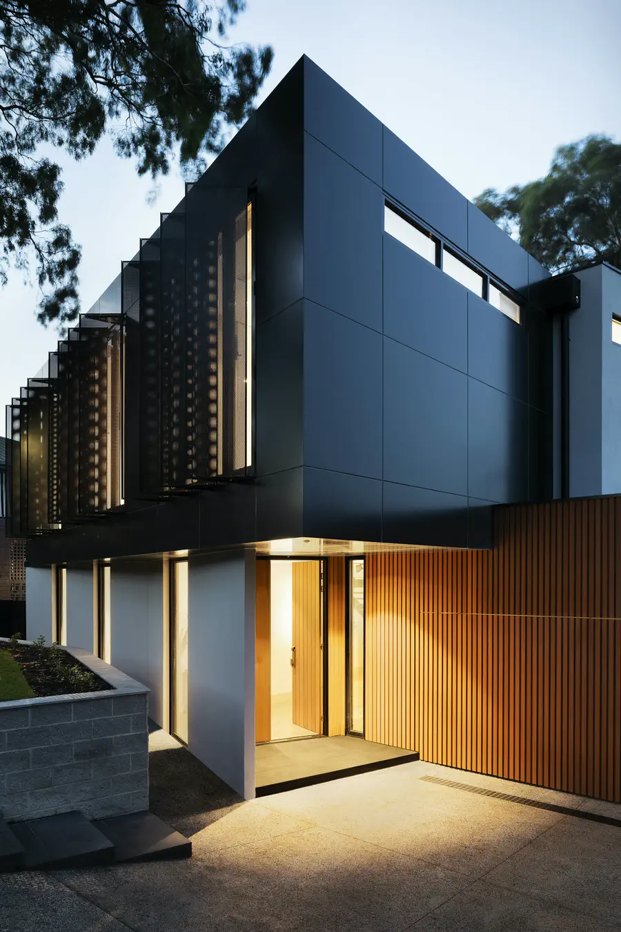 Façade noire d’une maison contemporaine au crépuscule, fenêtres éclairées